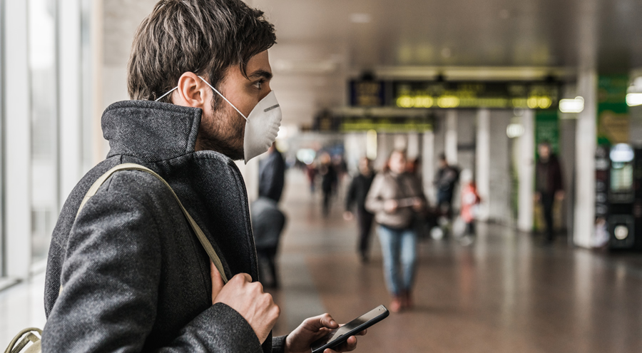 Man wearing protective mask using mobile phone in airport terminal